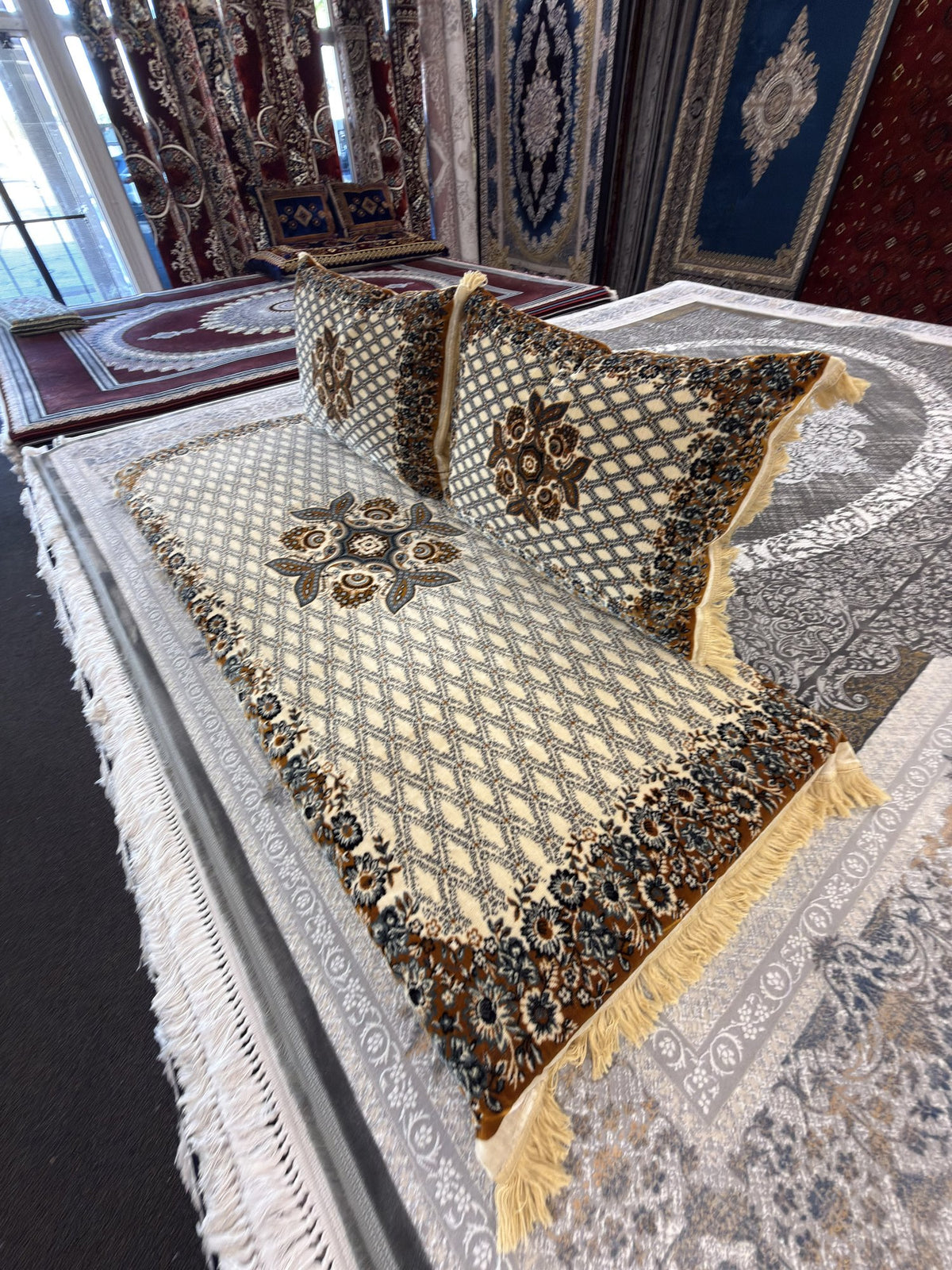 Ivory Afghan toshak with teal diamond lattice and rose cluster, angled view with two cushions