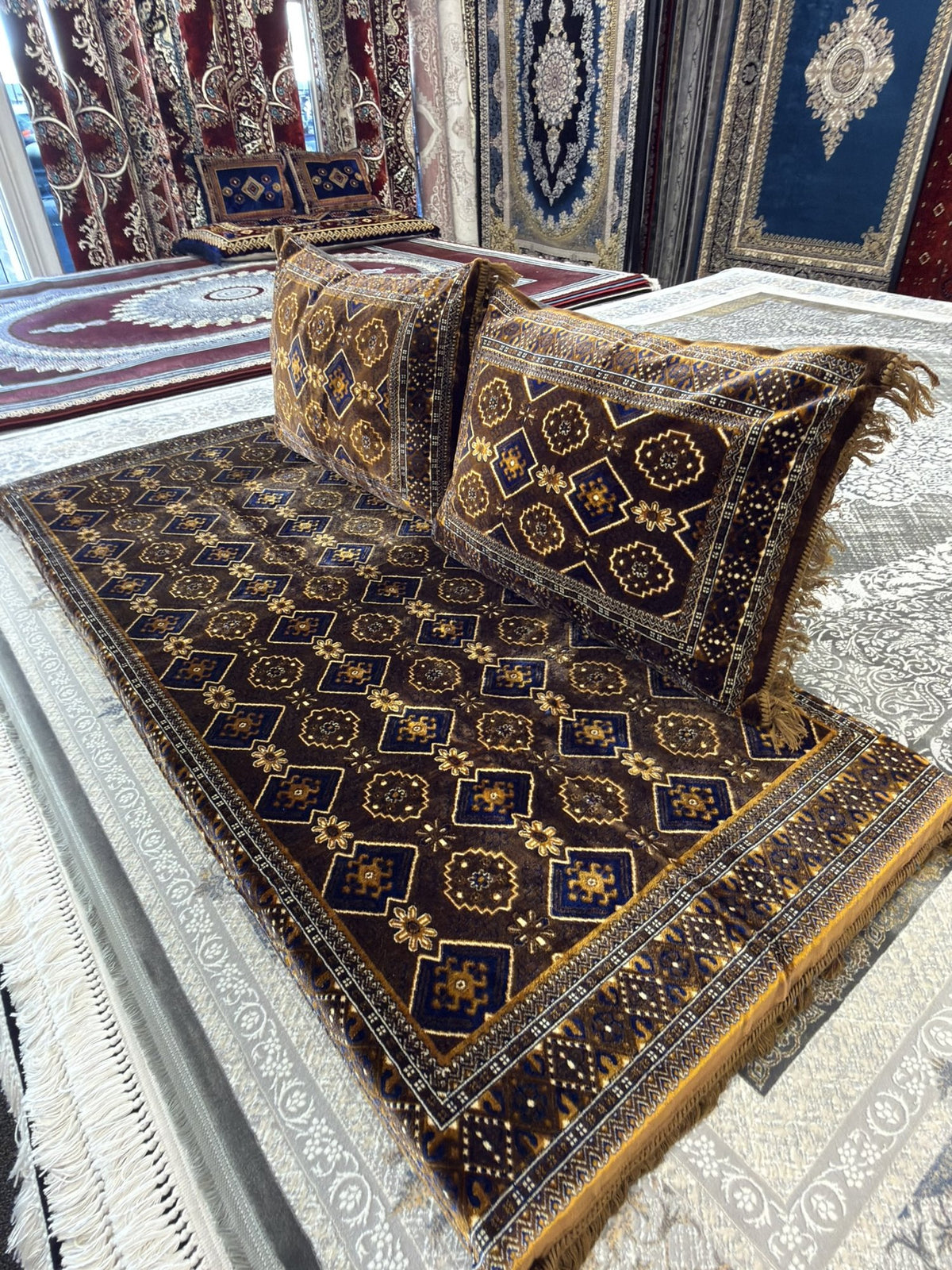 Deep brown Afghan toshak with repeating gold and blue Turkmen guls, angled view with cushions